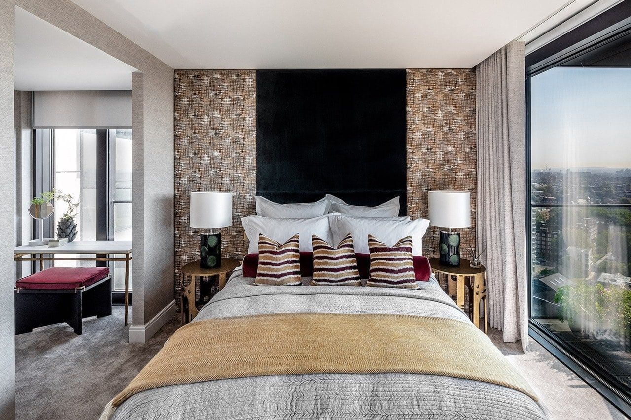 Bedroom with bed, nightstands, and window; gold and dark accents; desk in the background.