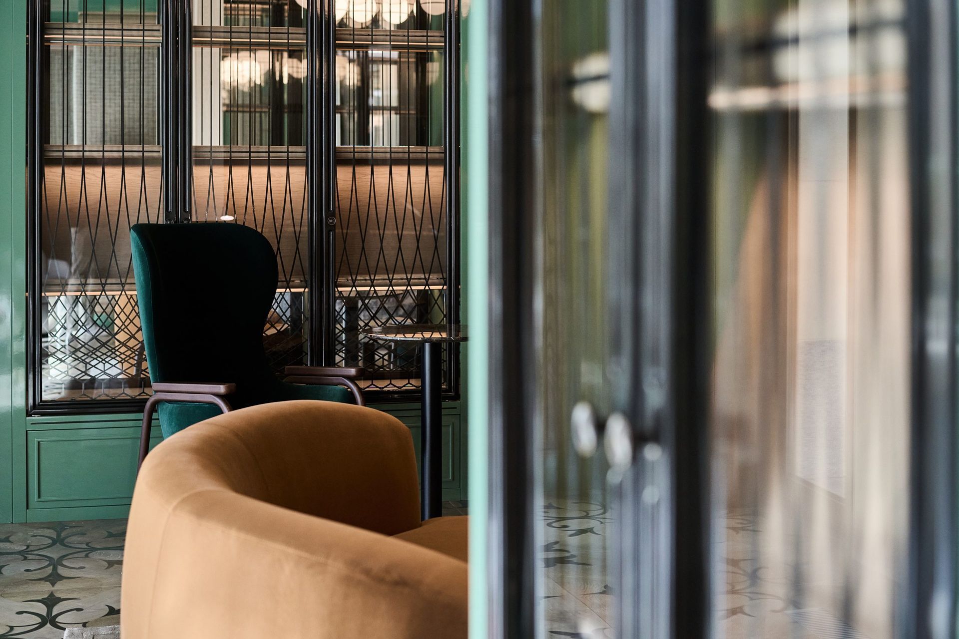 Cozy seating area with an amber armchair, a dark green wingback chair, and a glass-paneled cabinet in a room with green walls.