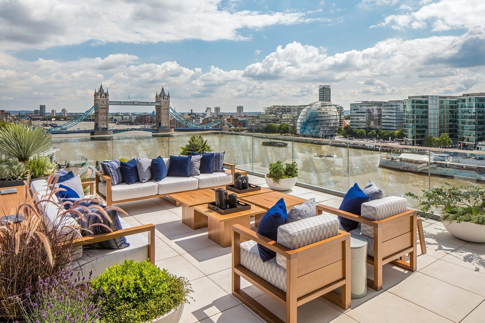 Rooftop patio with views of London's Tower Bridge and the Thames River; modern furniture with blue cushions.
