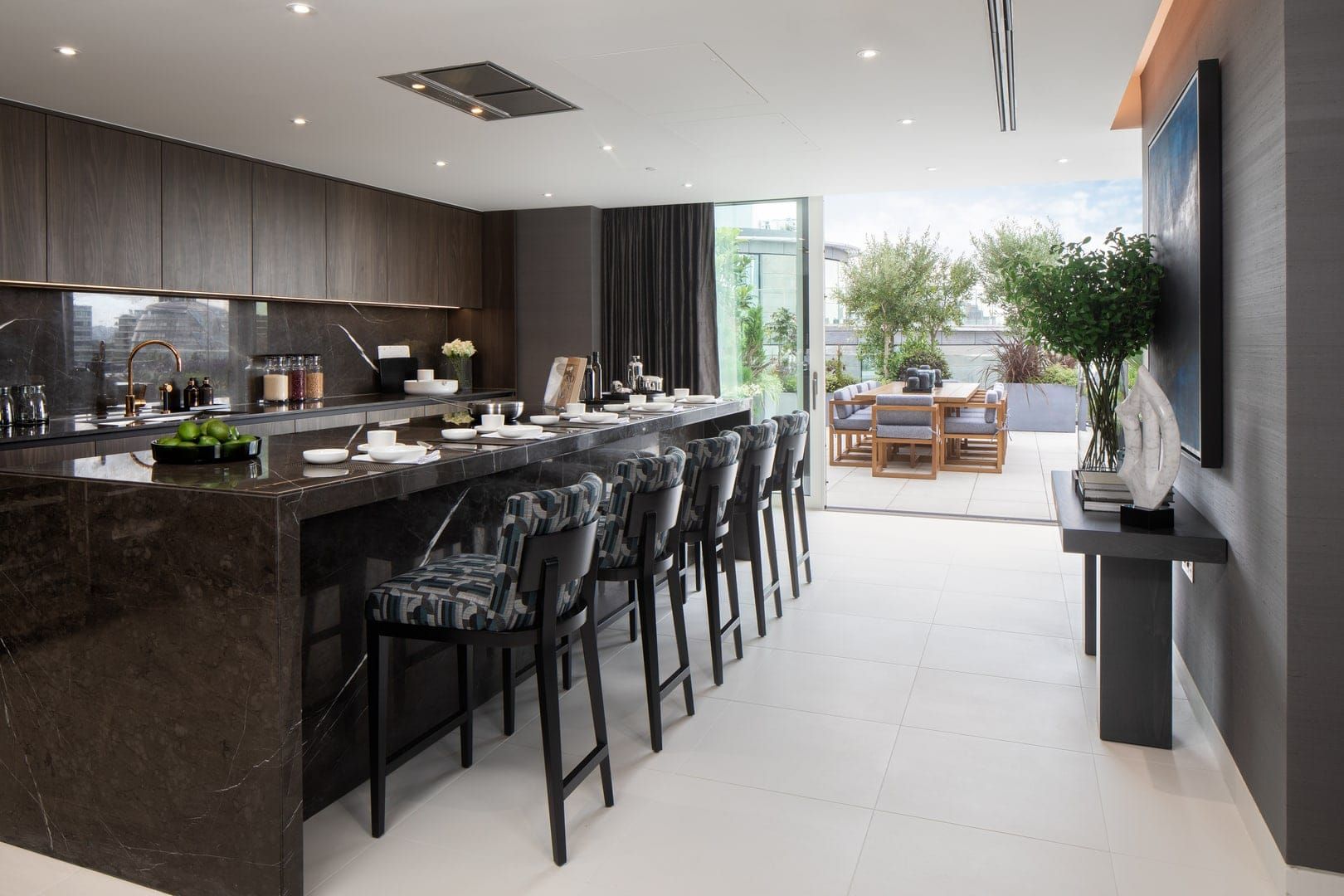 Modern kitchen with dark granite island and cabinets, leading to an outdoor dining area.
