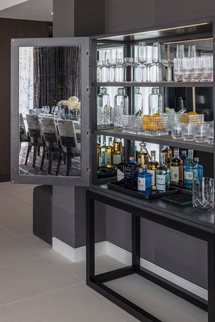 Gray bar cabinet with mirrored doors, stocked with glassware and liquor; dining room reflection.