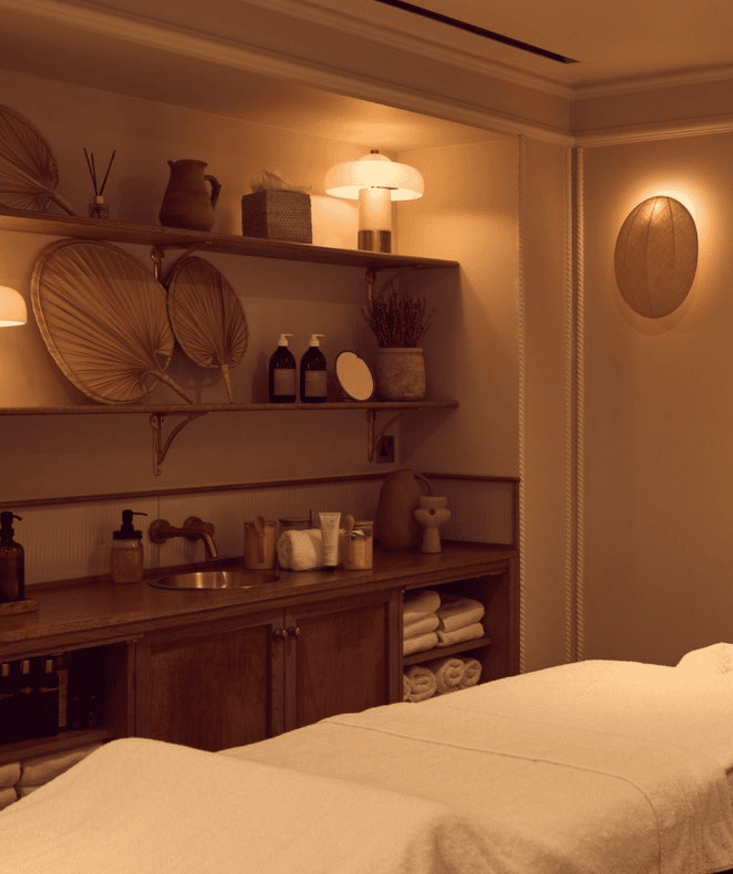 Massage therapy room: wooden shelves with products, a sink, and a massage table with white linens.