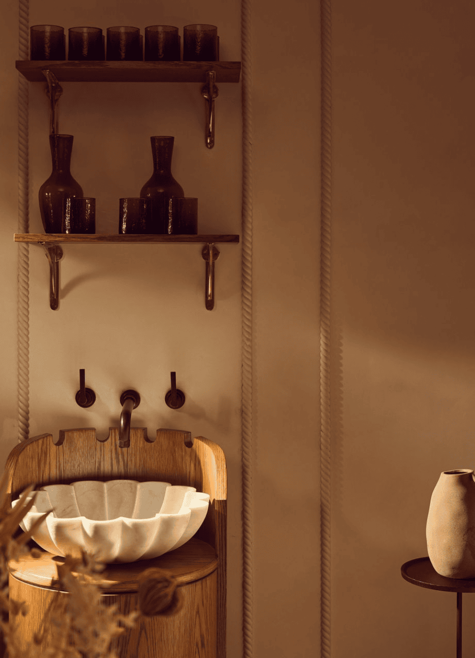 Wooden vanity with a shell-shaped sink, shelves with bottles, and a side table with a vase.