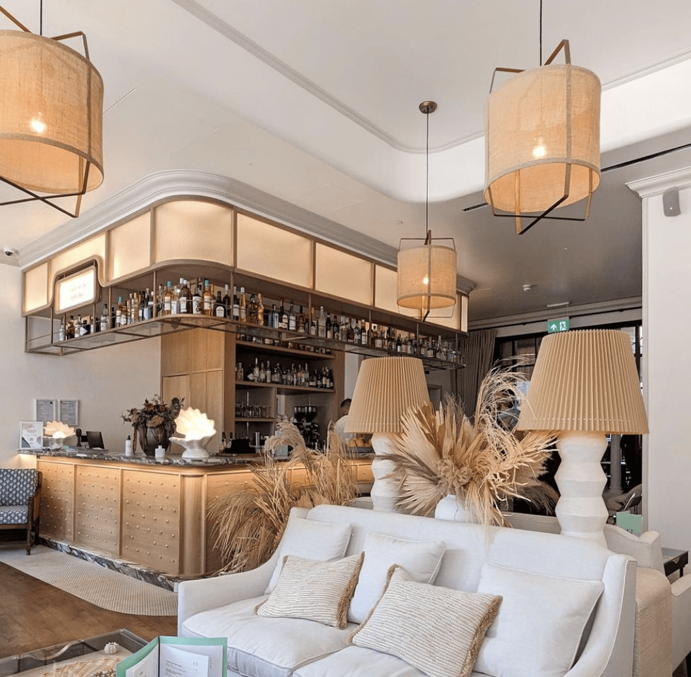 Bar interior with white couch, wooden bar, and hanging lamps.
