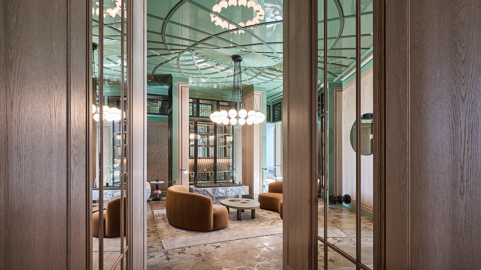 A luxury room through a doorway: aqua ceiling, chandeliers, brown chairs, and mosaic floor.