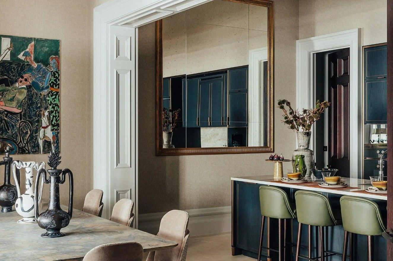 Elegant dining room with a long table, chairs, and a bar with stools. A large mirror reflects the room.