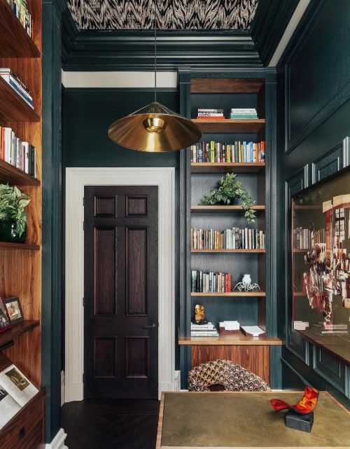Dark green home office with built-in shelves, wooden desk, and a gold pendant light.