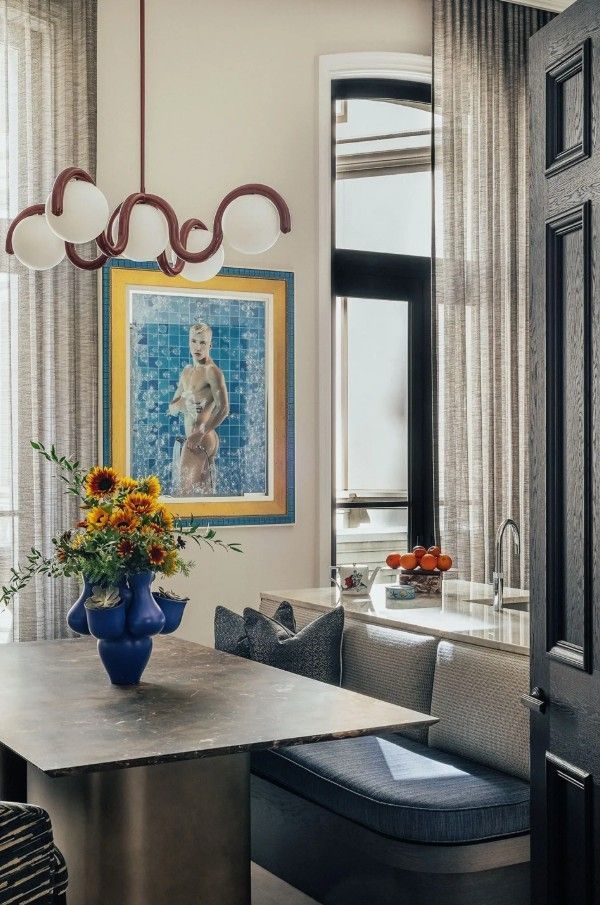 Dining area with floral arrangement, art, and chandelier. Built-in seating and tall window.