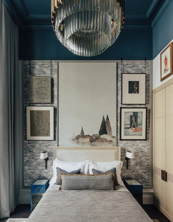 Bedroom with bed, artwork, blue walls, patterned wallpaper, and a crystal chandelier.