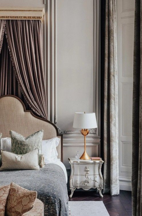 Elegant bedroom with canopy bed, ornate nightstand, and gold lamp.