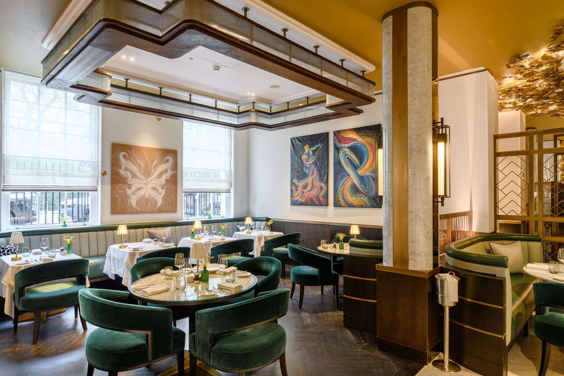 Elegant restaurant interior with round tables, green velvet chairs, and art.
