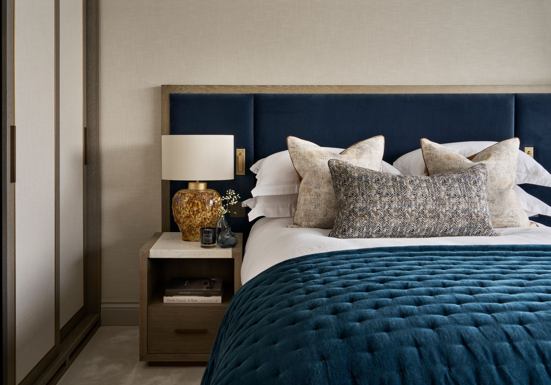 Bedroom with a blue bed, nightstand with lamp, and a wardrobe.