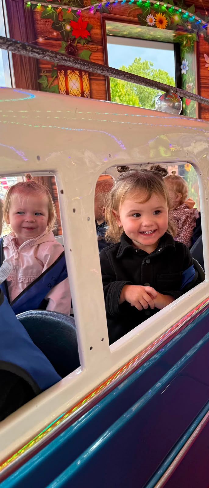 Twee lachende kinderen zitten in een kleurrijk karretje van een attractie in een pretpark