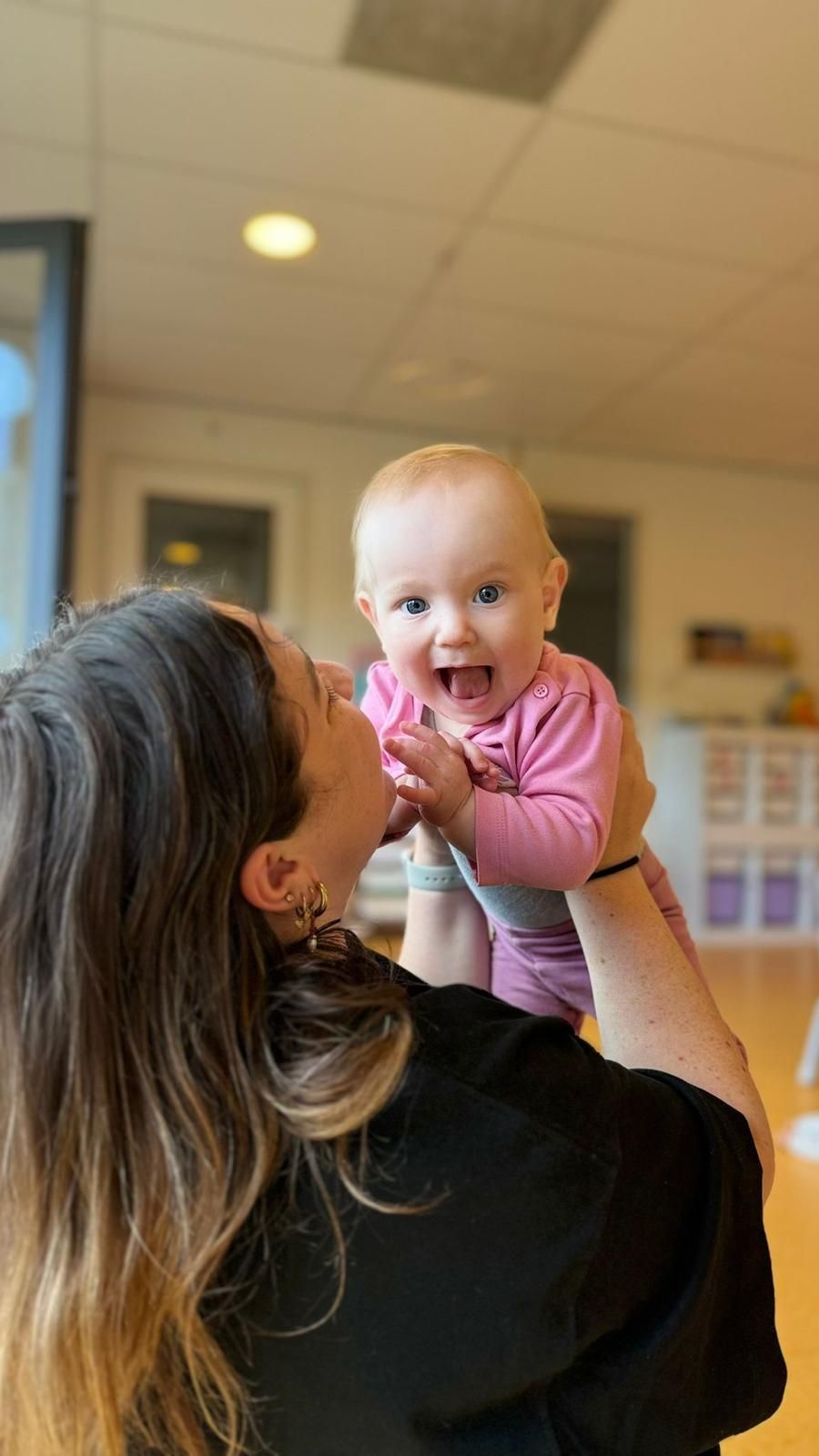 Een vrouw houdt een lachende baby vast in een lichte kamer