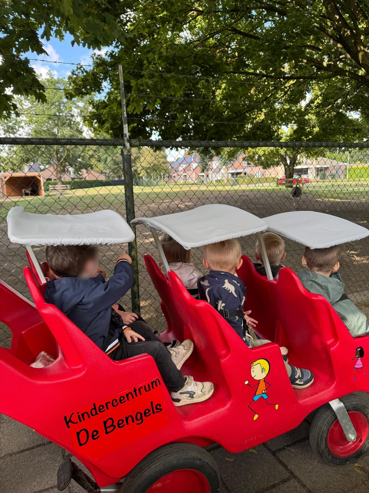 Kinderen rijden in een rode skelter onder de bomen op de speelplaats van een kleuterschool