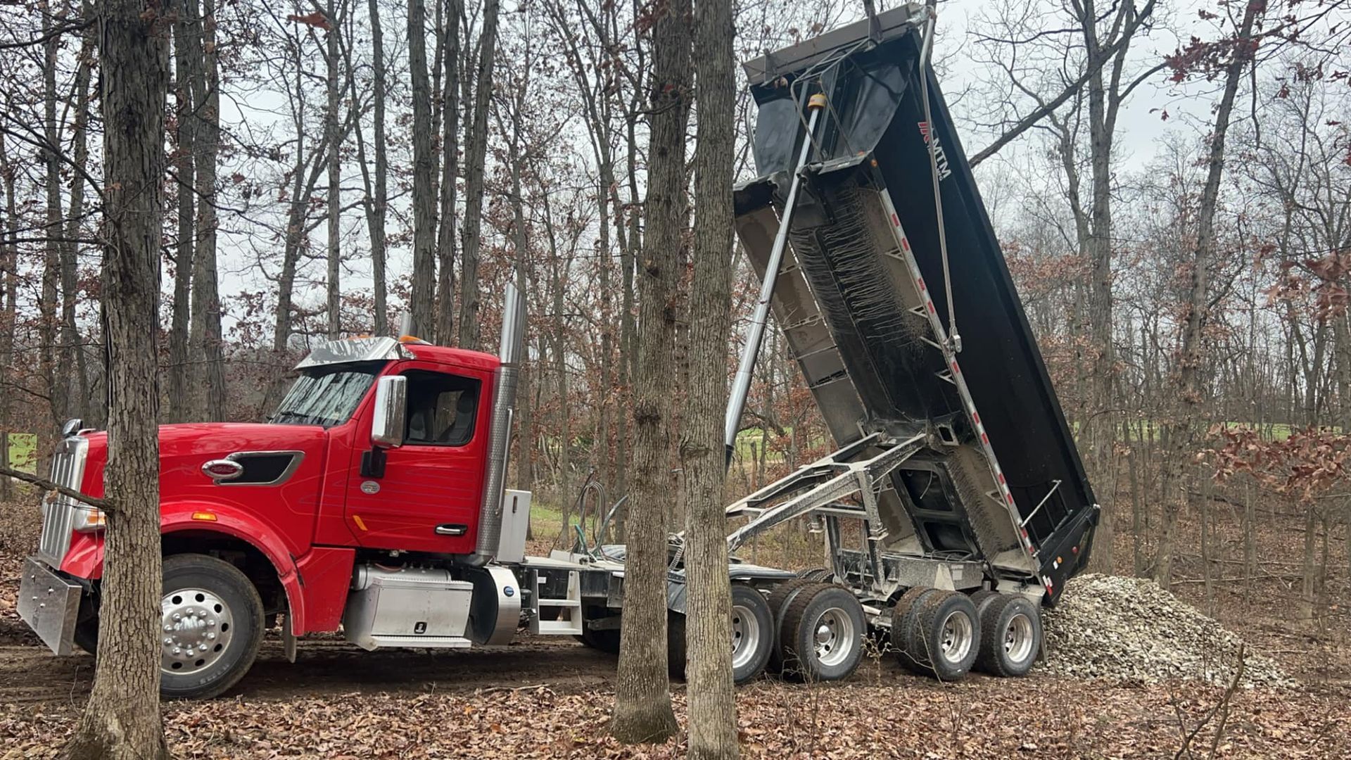 A red dump truck is parked in the middle of a forest.
