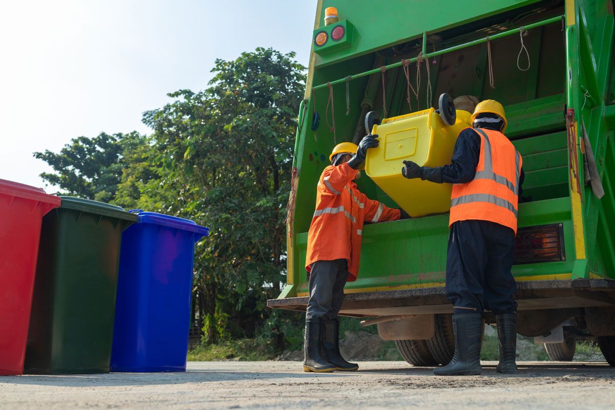 Two men are loading a yellow trash can into a garbage truck.
