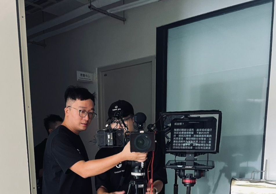 兩個人正在灰色的走廊上用架在三腳架上的攝影機拍攝。
