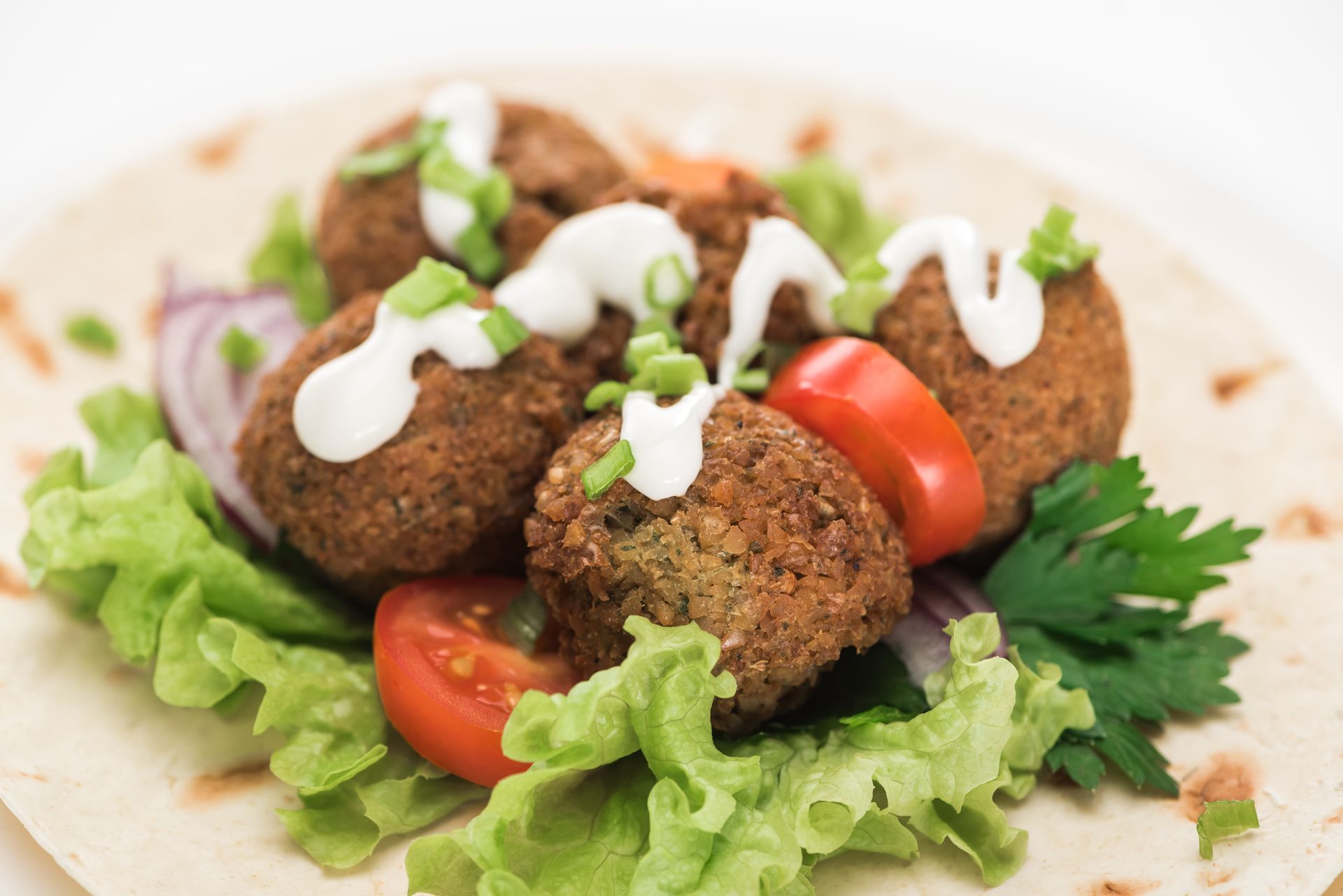 a close up of a plate of food with falafel , tomatoes , lettuce and sauce on a tortilla .