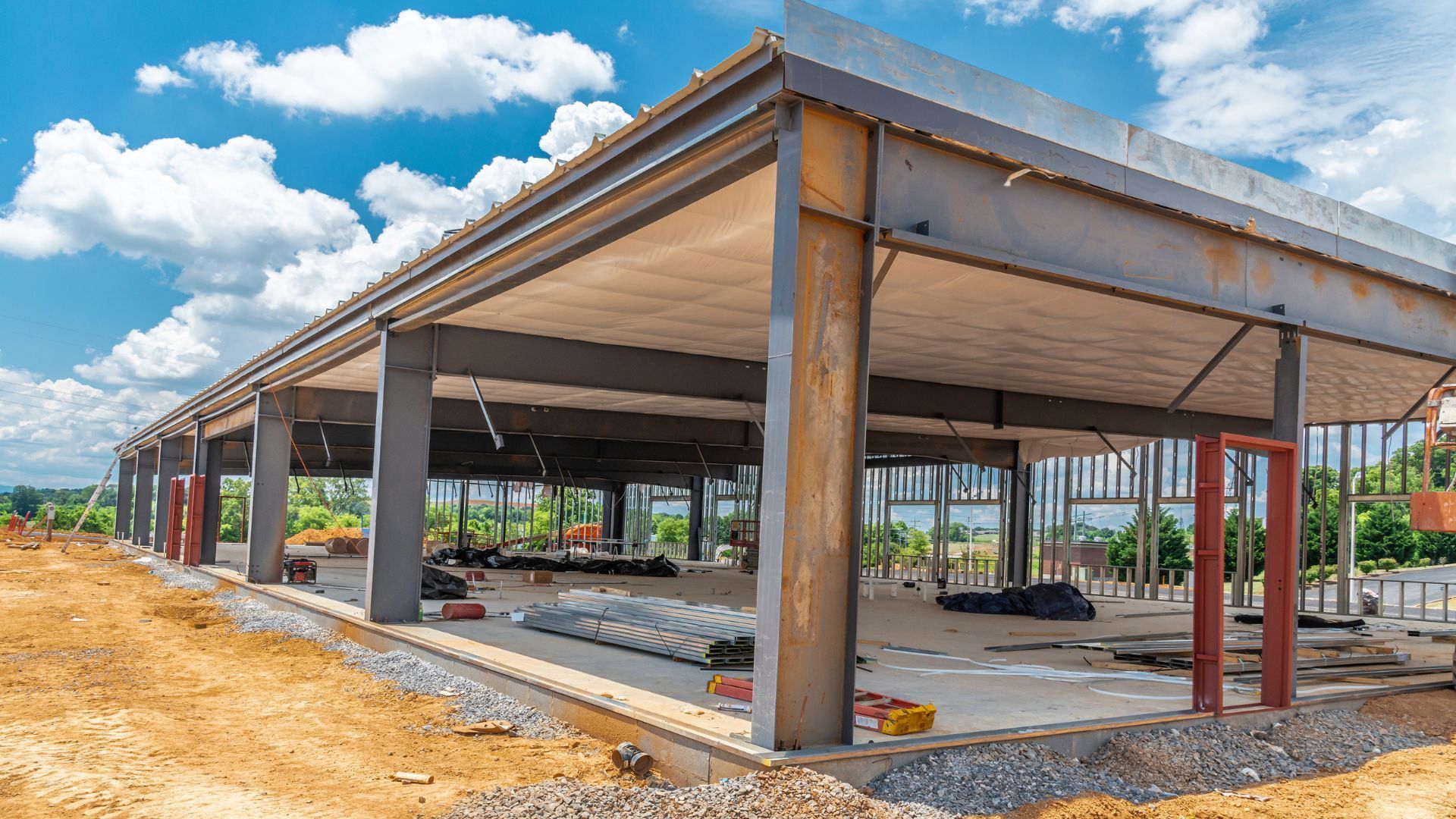 Construction of a building with concrete floor and steel frame, under a cloudy blue sky.