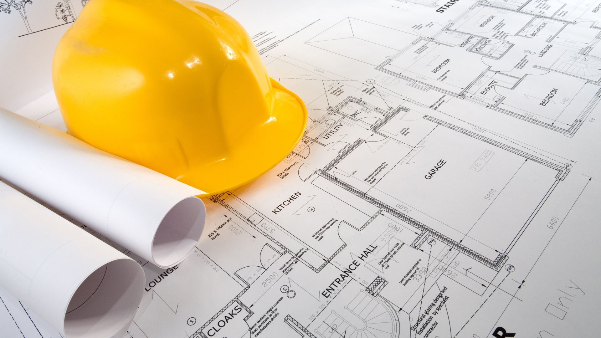 Yellow hard hat on architectural blueprints, with rolled-up paper.