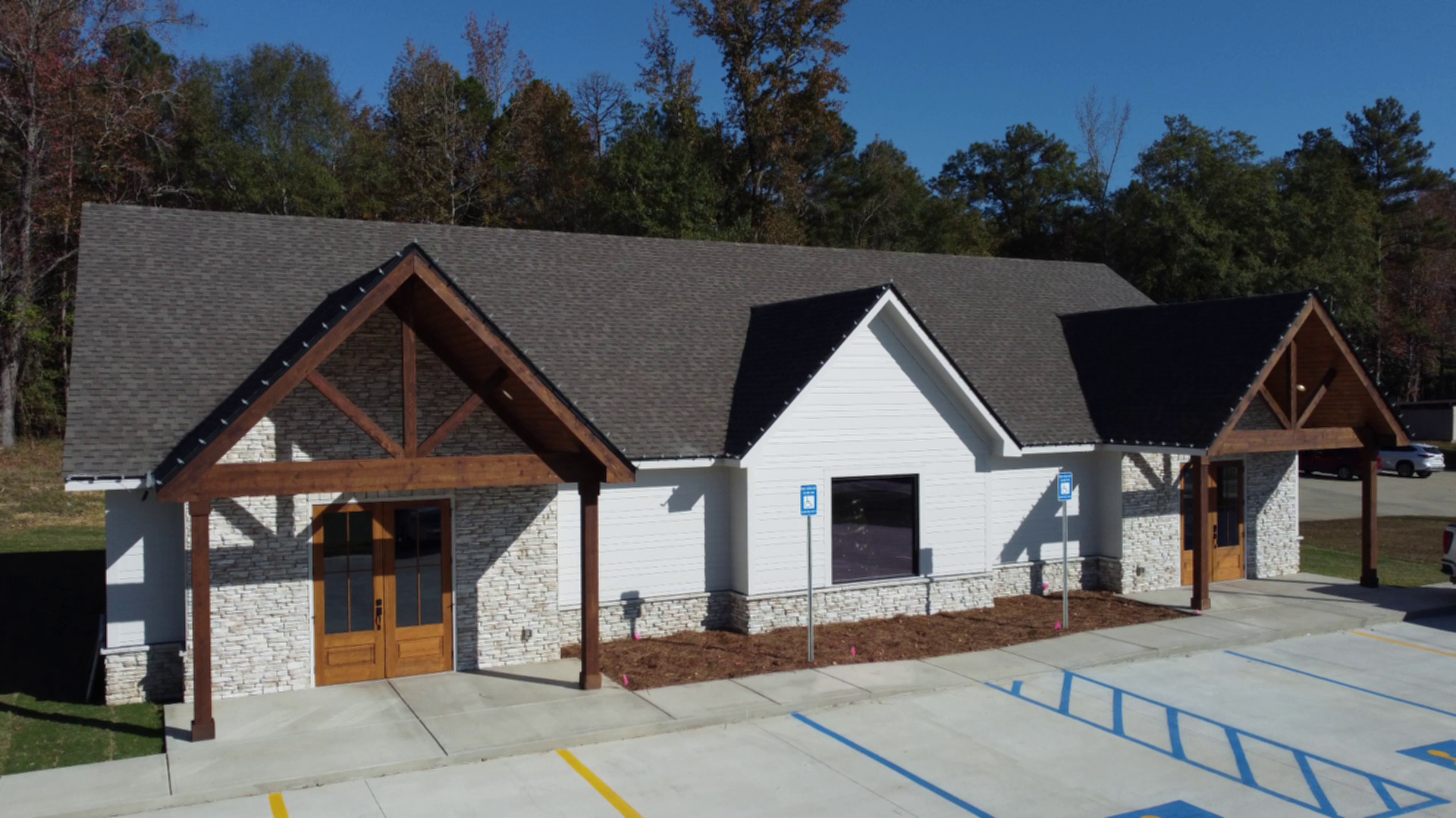 White building with dark gray roof, two wooden-framed entrances, and handicap parking spaces in front.