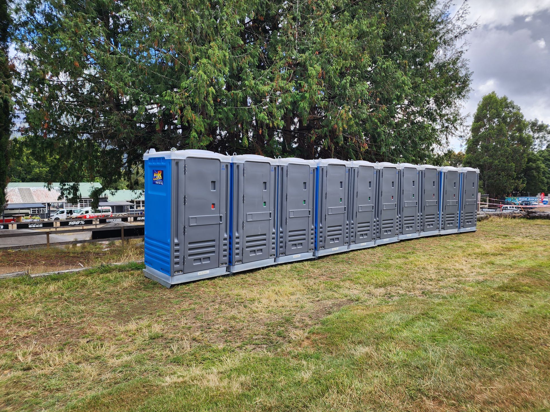 Row of gray and blue portable toilets on a grassy lot under trees — Wee R Pumping In Glenorchy, TAS
