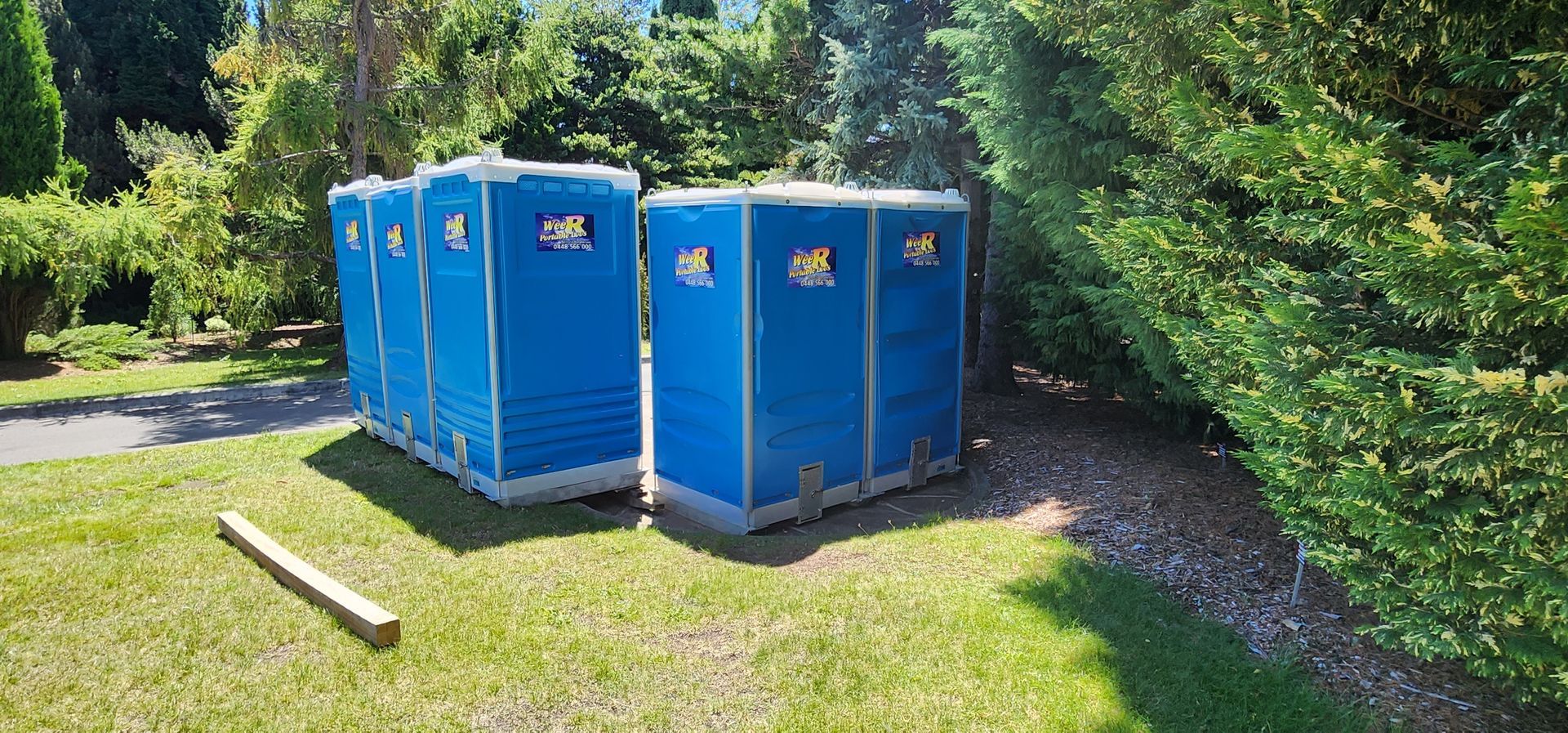 Blue portable toilets lined up on grass beside a wooded path — Wee R Pumping In Glenorchy, TAS