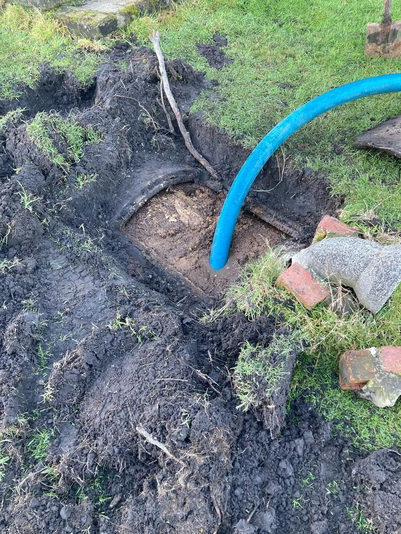 Blue hose in muddy dug hole beside exposed roots and a few red bricks in grassy yard— Wee R Pumping In Glenorchy, TAS