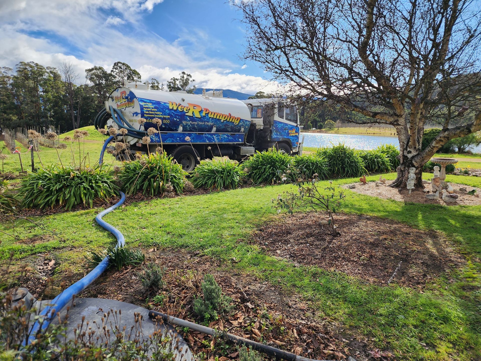 Blue Utility Truck by a Lake, With a Hose Across a Grassy Yard and Trees — Wee R Pumping In Glenorchy, TAS