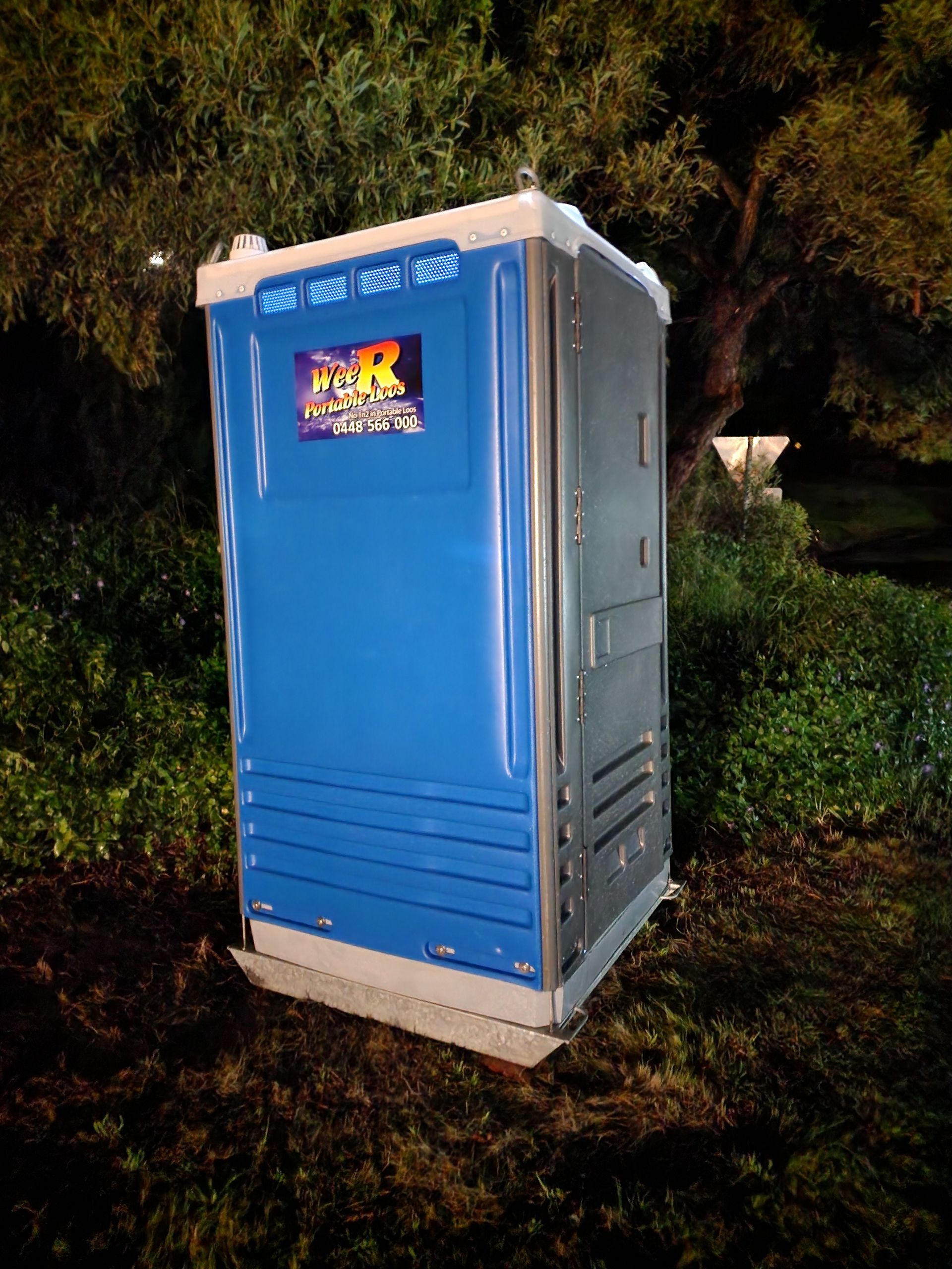 Blue portable toilet outdoors at night beside trees and bushes — Wee R Pumping In Glenorchy, TAS