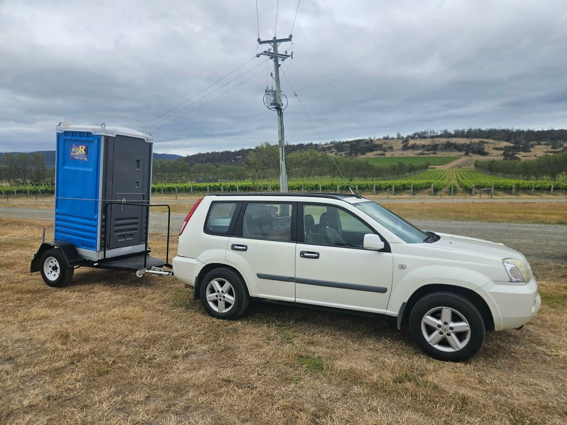 White SUV towing a blue enclosed trailer in a rural field under an overcast sky — Wee R Pumping In Glenorchy, TAS