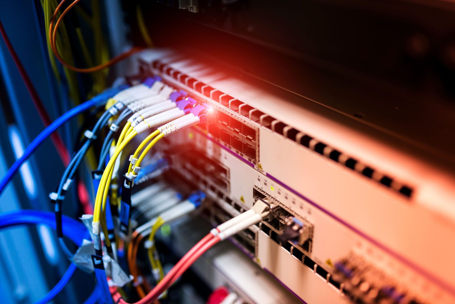 Close-up of a server rack with many colored cables connected to networking hardware, lit with red light. Close-up of a server rack with many colored cables connected to networking hardware, lit with red light.
