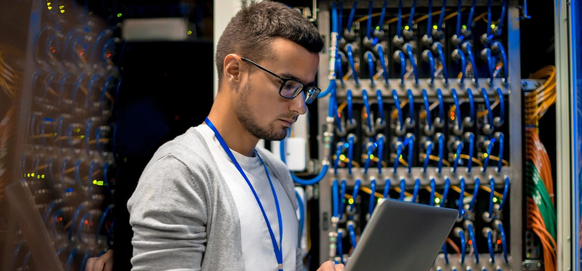 Man with glasses using a laptop in a server room, looking at servers, cable management. Man with glasses using a laptop in a server room, looking at servers, cable management.