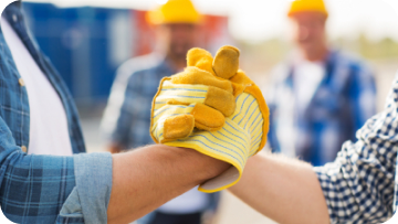 Two construction workers bump gloved hands, others in background. Two construction workers bump gloved hands, others in background.