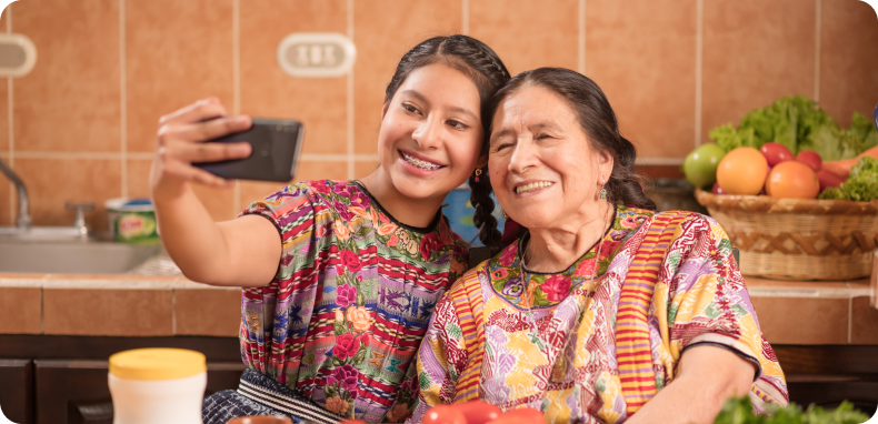 Young woman taking a selfie with an older woman in a kitchen, both smiling. Young woman taking a selfie with an older woman in a kitchen, both smiling.