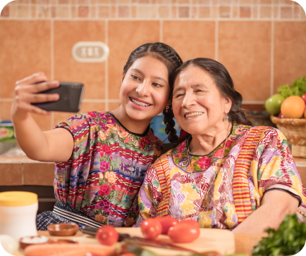 Young woman and older woman in colorful blouses taking a selfie in a kitchen.