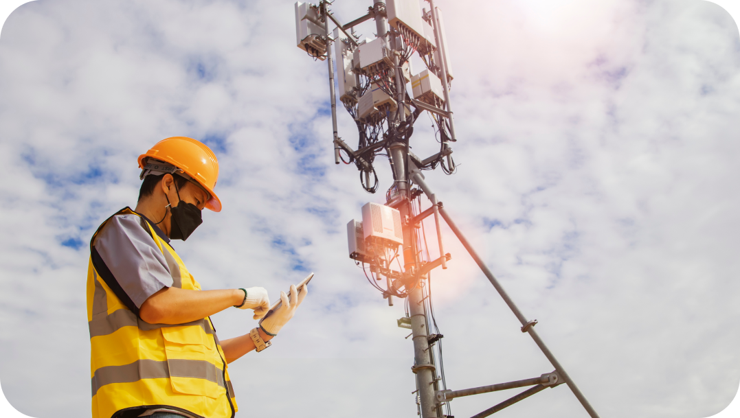 Worker in safety gear inspecting a cell tower, with a cloudy sky in the background. Worker in safety gear inspecting a cell tower, with a cloudy sky in the background.