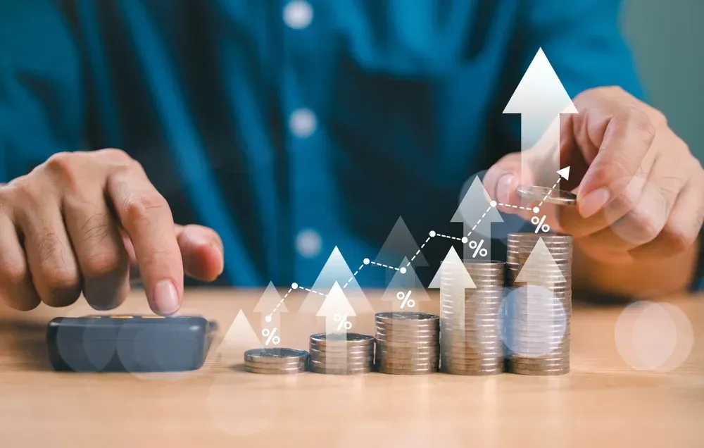 Person calculating, with growing stacks of coins and a rising stock chart. Person calculating, with growing stacks of coins and a rising stock chart.