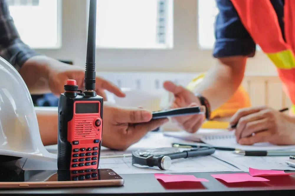Close-up: Radio on desk, two people discussing plans. Construction site, workspace. Close-up: Radio on desk, two people discussing plans. Construction site, workspace.