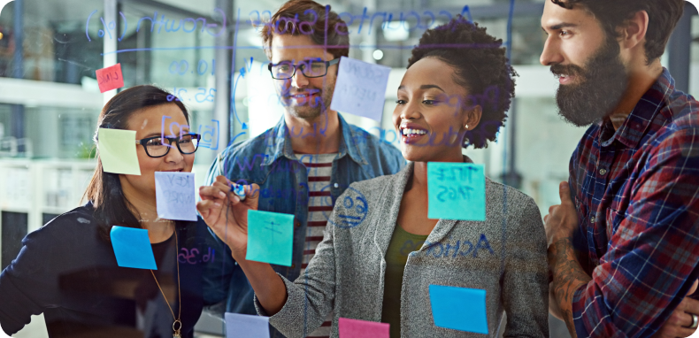 Four people in a collaborative brainstorming session, using sticky notes on a glass wall. Four people in a collaborative brainstorming session, using sticky notes on a glass wall.