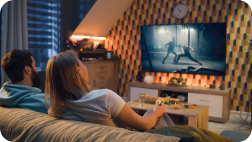 Couple on sofa watching action movie on TV, warm-lit room. Couple on sofa watching action movie on TV, warm-lit room.