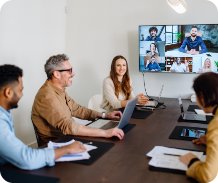 People in a meeting room having a video call with remote colleagues on a large screen. People in a meeting room having a video call with remote colleagues on a large screen.