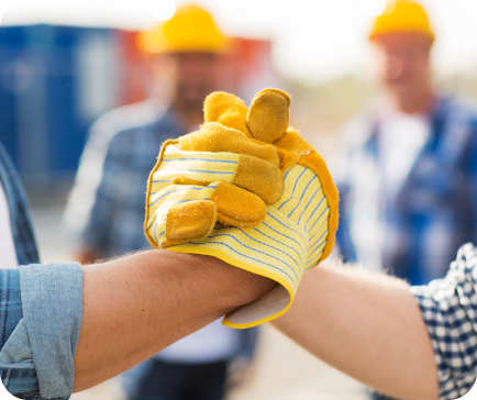 Three construction workers doing a fist bump, one with a work glove, on a construction site. Three construction workers doing a fist bump, one with a work glove, on a construction site.