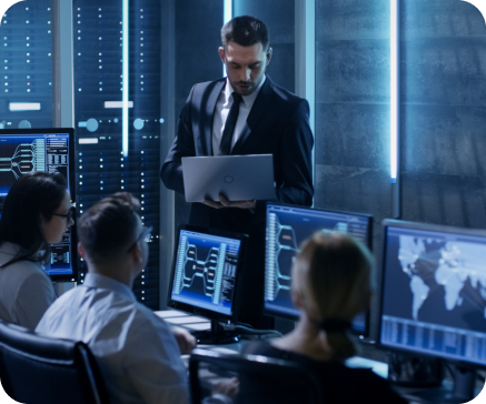 Group of people in a server room, looking at computer monitors. A man in a suit presents with a laptop. Group of people in a server room, looking at computer monitors. A man in a suit presents with a laptop.