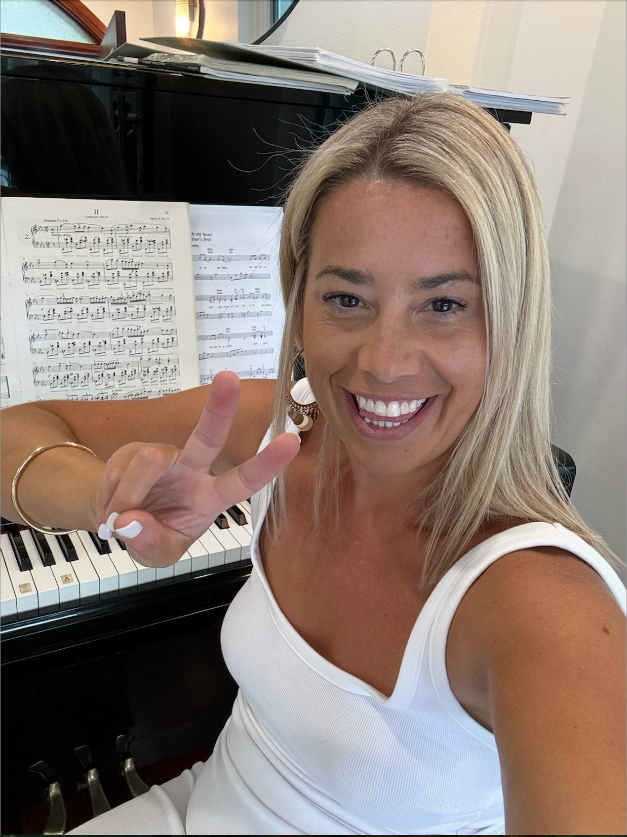 Lindsay Gilroy is sitting in front of a piano giving a peace sign