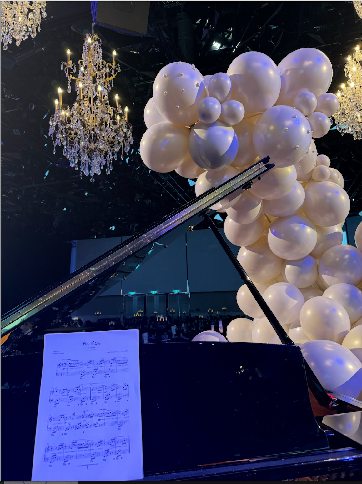 A piano is surrounded by white balloons and a sheet of music