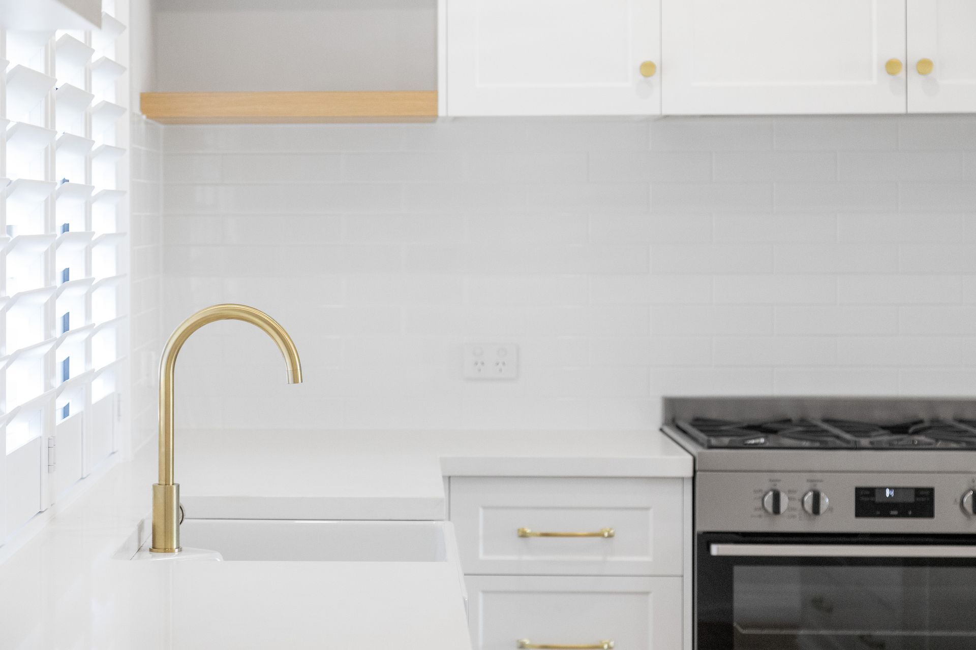 Bright white kitchen with gold faucet, white cabinets, and stainless steel stove
