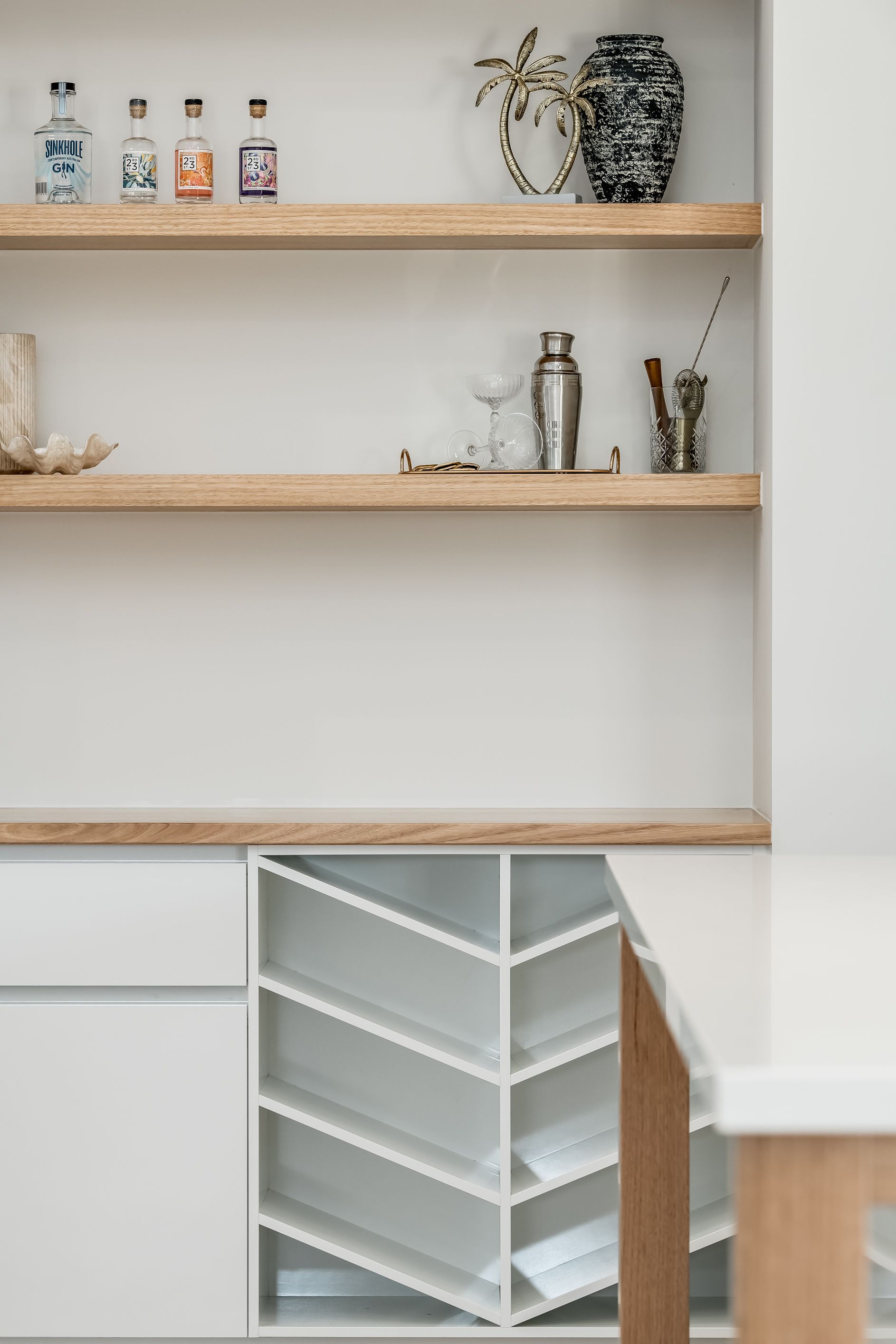 Minimalist kitchen shelves with jars and plants above a white cabinet with a built-in angled wine rack