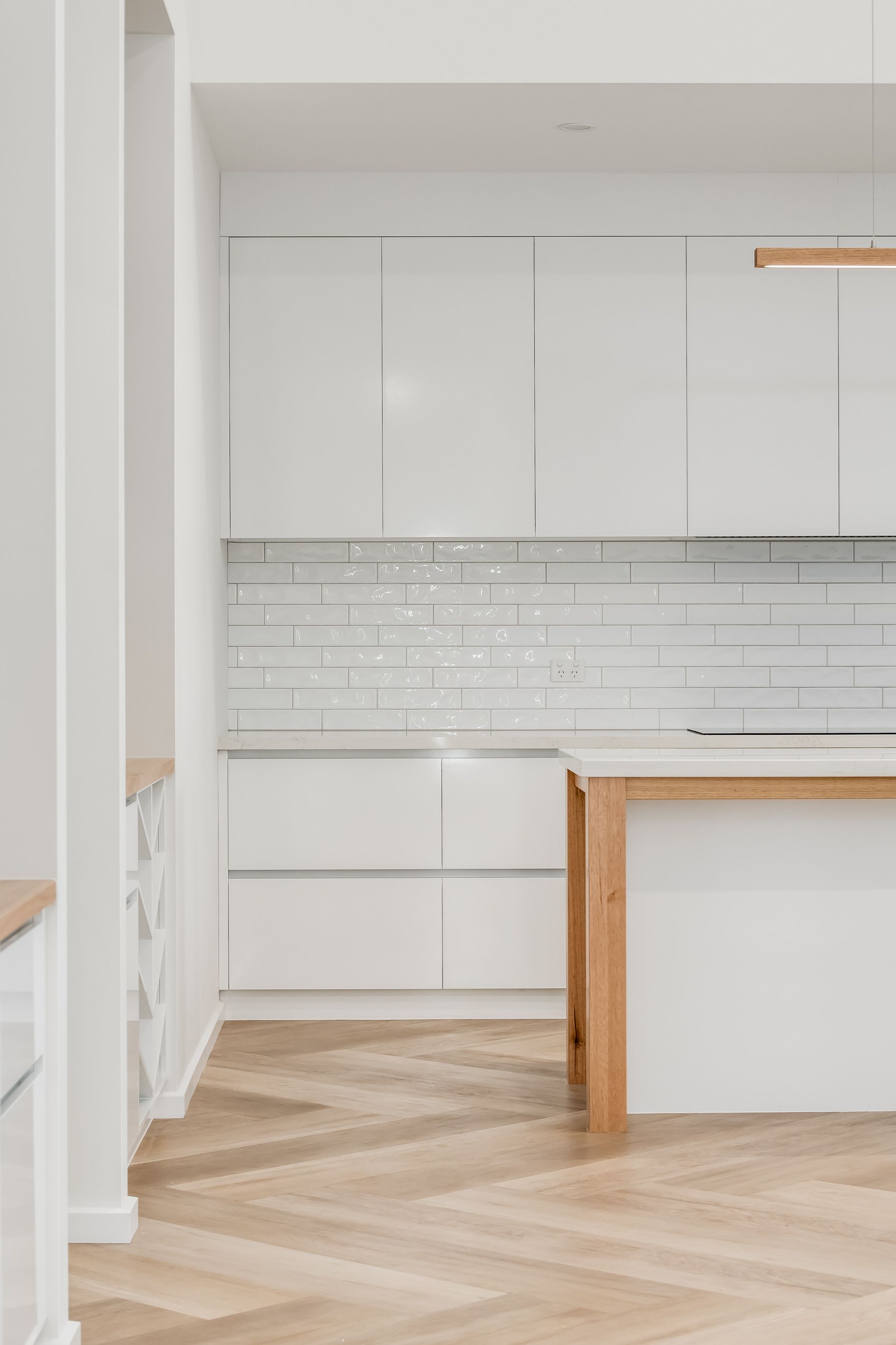 Bright white minimalist kitchen with glossy cabinets, subway tile backsplash, and herringbone wood floor